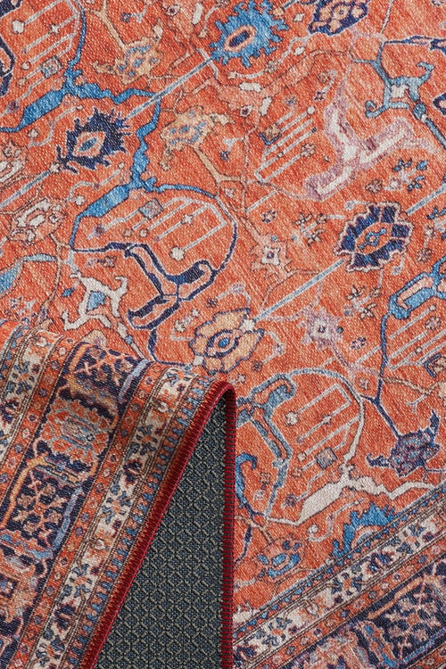 Load image 1 in gallery view. The Aurelius Coral Washable Rug - LCC3005 features a vibrant orange Persian-style flat weave with intricate blue and white patterns, shown with a folded corner revealing its detailed underside—ideal for high-traffic spaces.