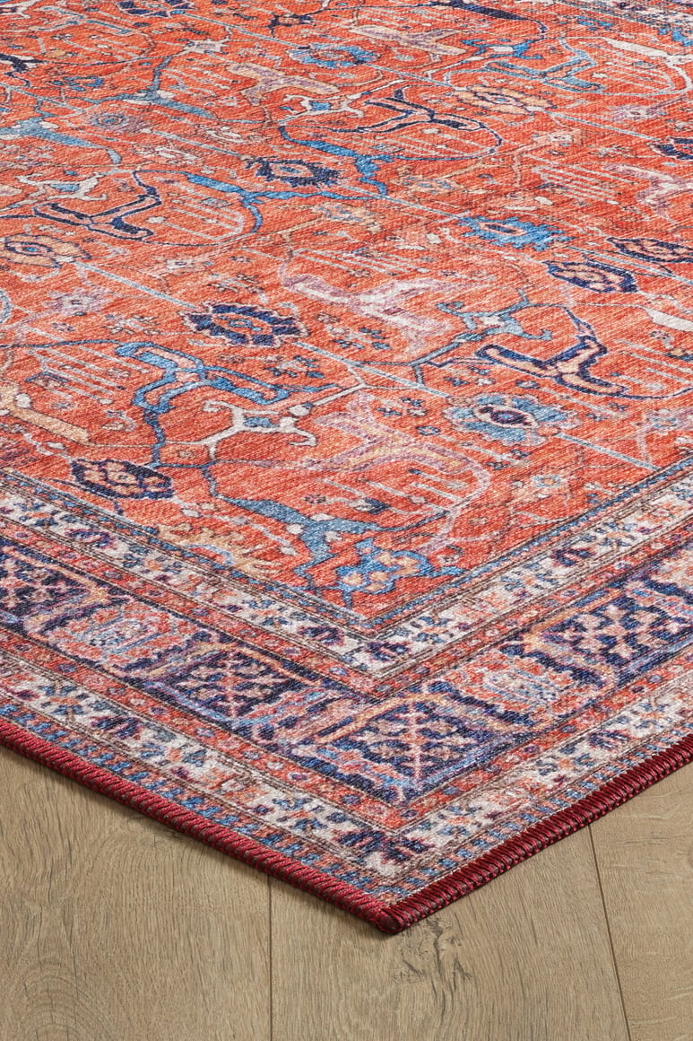 A close-up of the Aurelius Coral Washable Rug - LCC3005, featuring red flat weave with blue and white patterns and a purple border, displayed on a light wood floor—perfect for high-traffic spaces.