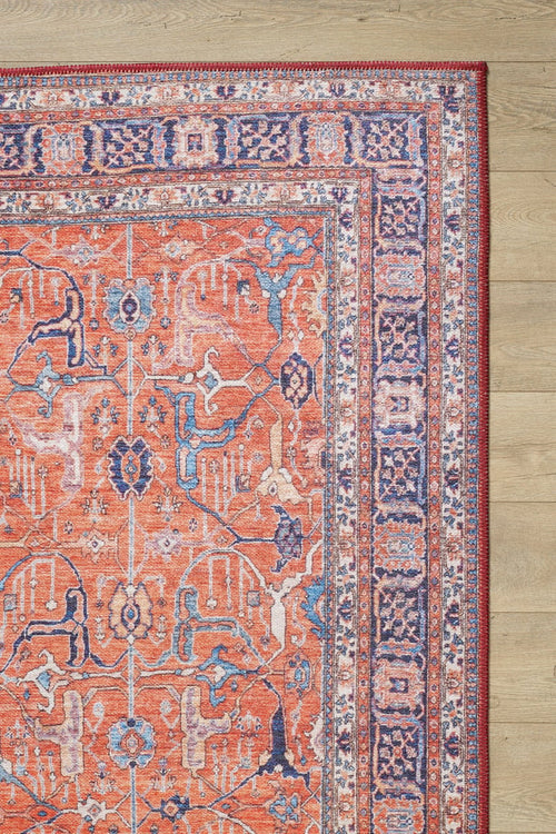Load image 1 in gallery view. A corner of the Aurelius Coral Washable Rug - LCC3005, featuring vibrant orange, blue, and cream geometric and floral patterns, lies on a light wood floor. This durable flat weave style is ideal for high-traffic areas.
