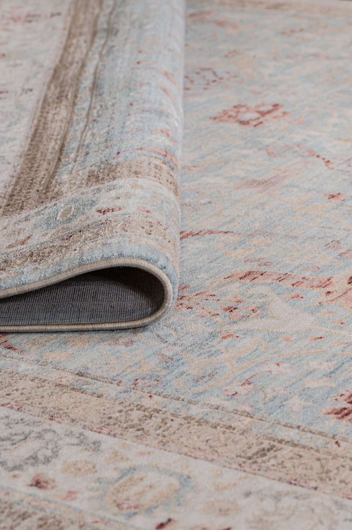 A close-up of the Azure Oushak Area Rug (APX2932) showcases its soft blue, beige, and reddish patterns, with one edge folded to reveal the underside of this vintage-inspired rug.