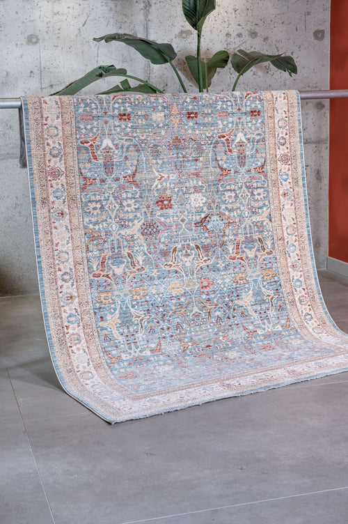 Load image 1 in gallery view. The Azure Oushak - Area Rug - APX2932 in blue, white, and red drapes over an indoor metal railing, with a green leafy plant and concrete wall visible in the background.
