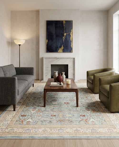 Load image 1 in gallery view. A modern living room with a gray sofa, two green armchairs, a wooden coffee table, and the Azure Oushak - Area Rug - APX2932. A floor lamp stands in the corner. Above the white marble fireplace hangs an abstract navy and gold painting.
