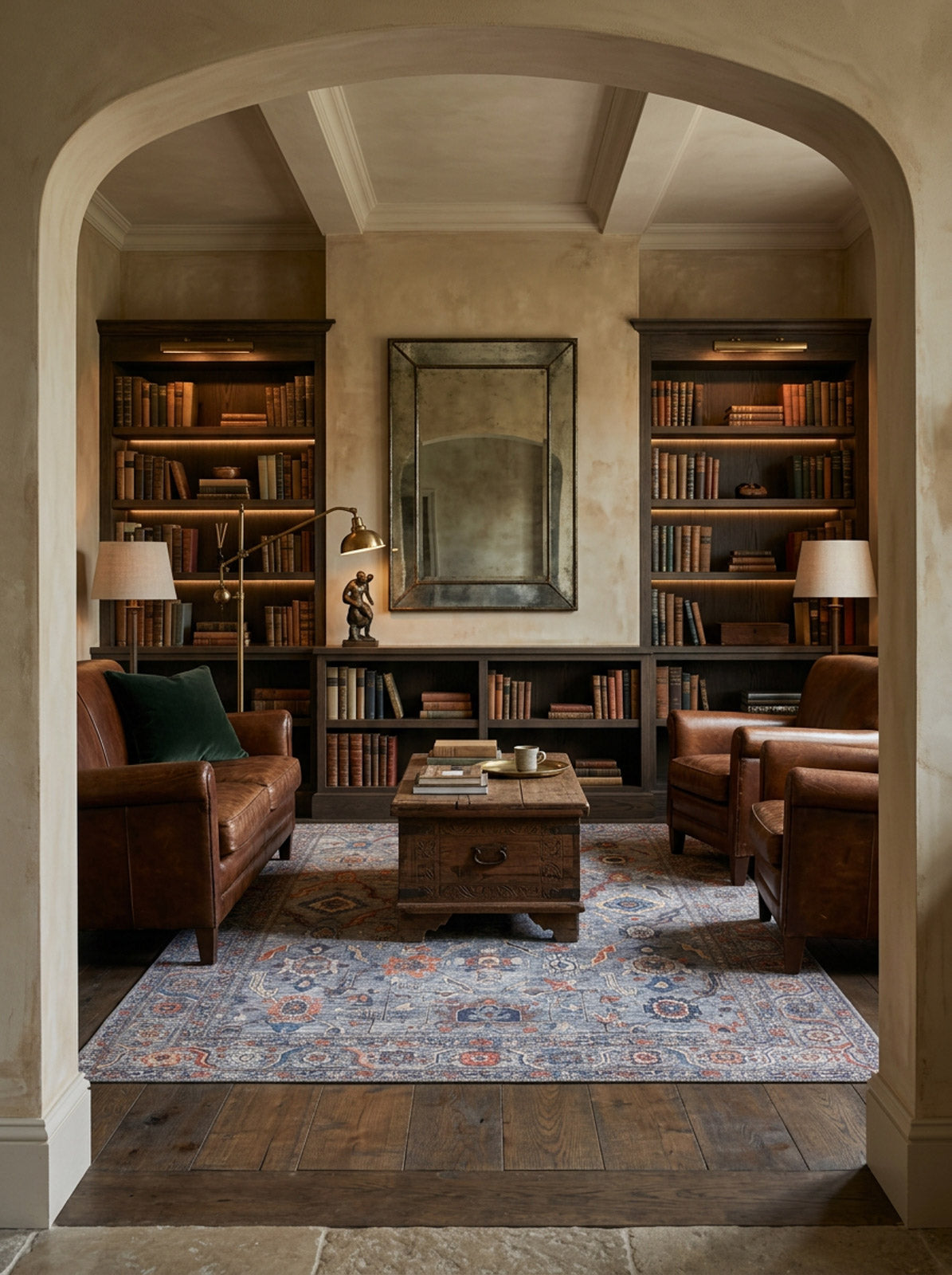 Blue and rust-toned traditional medallion rug in a library setting with leather armchairs and dark wood bookshelves.