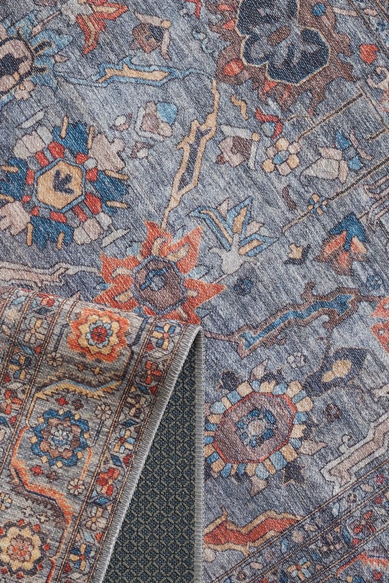 A close-up of the Bellaris Gray Washable Rug - LCC3003 (Custom Size) shows floral and geometric patterns in blue, orange, and beige. A folded corner reveals its textured underside; this allergy-friendly rug is both stylish and practical.