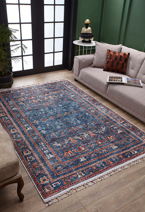 Load image 1 in gallery view. A living room with the Berber Beauty - Washable Rug - JR5092 (Custom Size), blue with red and cream patterns on wooden floors, a light gray sofa, round side table, green walls, and large windows—ideal for high-traffic spaces.