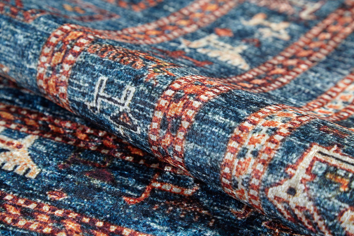 A close-up of the Berber Beauty - Washable Rug - JR5092 (Custom Size) reveals intricate red and cream geometric designs on blue, shown folded to highlight its detailed texture—ideal for high-traffic areas.
