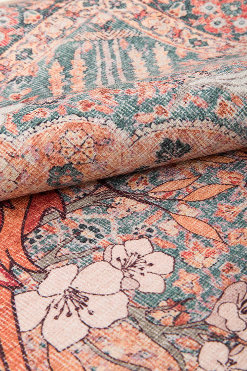 Bild 1 in Galerieansicht laden. A close-up of the Blazefang Myth - Washable Rug (JR0049), a flat weave rug with intricate floral and geometric designs in muted orange, green, cream, and brown tones, shown with one edge slightly folded.