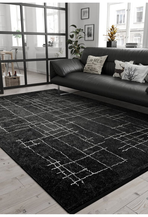 Load image 1 in gallery view. Modern living room with the Bohemian Illusion - Washable Rug - JR1953, black leather sofa with patterned cushions, light wood floor, potted plants, and large windows for natural light. Minimalist decor in monochrome tones.