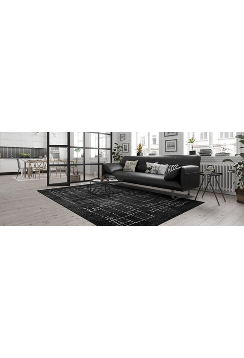 Load image 1 in gallery view. Modern living room featuring a black sofa, patterned cushions, Bohemian Illusion - Washable Rug - JR1953, small round coffee table, potted plants, and wall art, with the dining area and kitchen visible in the background.