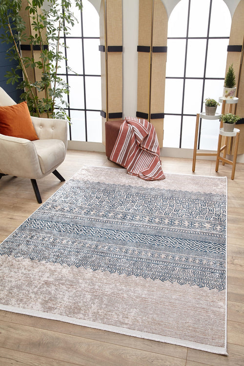 Load image 1 in gallery view. A modern living room features the Bohemian Nights - Washable Rug - JR1585 (Custom Size), ideal for high-traffic areas, a cream armchair with orange pillows, a brown pouf with a striped blanket, potted plants, and bright arched windows.