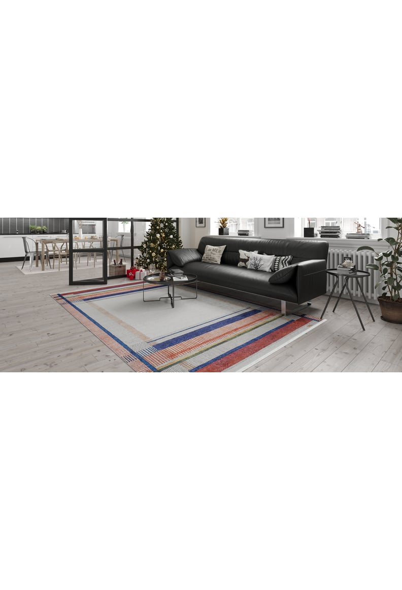 A modern living room featuring a black sofa, Bohemian Nightscape - Washable Rug - JR1701 in red, a coffee table, a decorated Christmas tree by the window, indoor plants, and a bright dining area—ideal for high-traffic spaces.