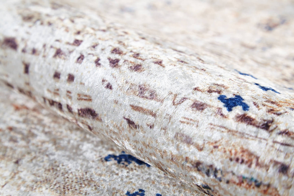A close-up of the Boho Babe - Washable Rug - JR1664 (Custom Size) shows its textured, rolled surface and beige, brown, and blue abstract pattern. The soft, slightly shiny fabric is perfect for high-traffic areas and showcases subtle color variations.