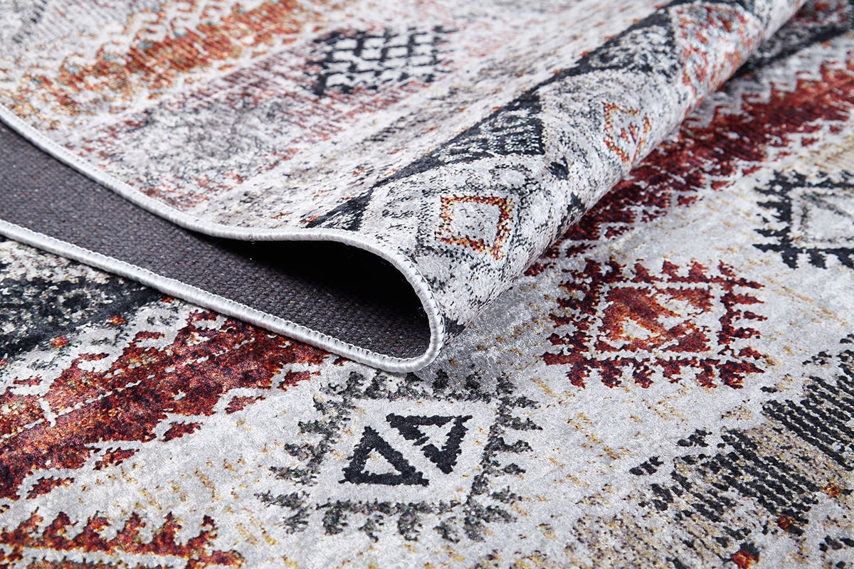 A close-up of the Boho Oasis - Washable Rug - JR1618 (Custom Size) shows its red, orange, black, and gray geometric design and textured underside—durable and ideal for high-traffic areas.