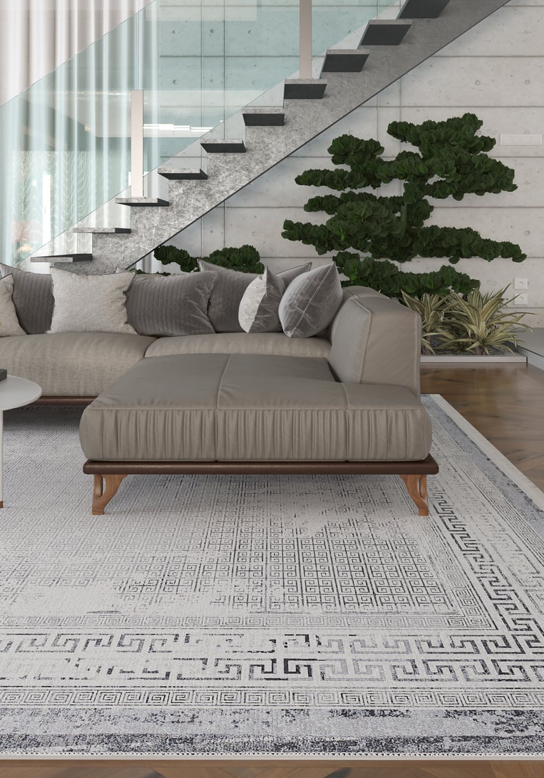 Modern living room with a grey sectional sofa, Bold Borderline - Washable Rug - JR1984 (custom size) ideal for high-traffic areas, decorative pillows, a glass staircase, and green indoor plants against a concrete wall.