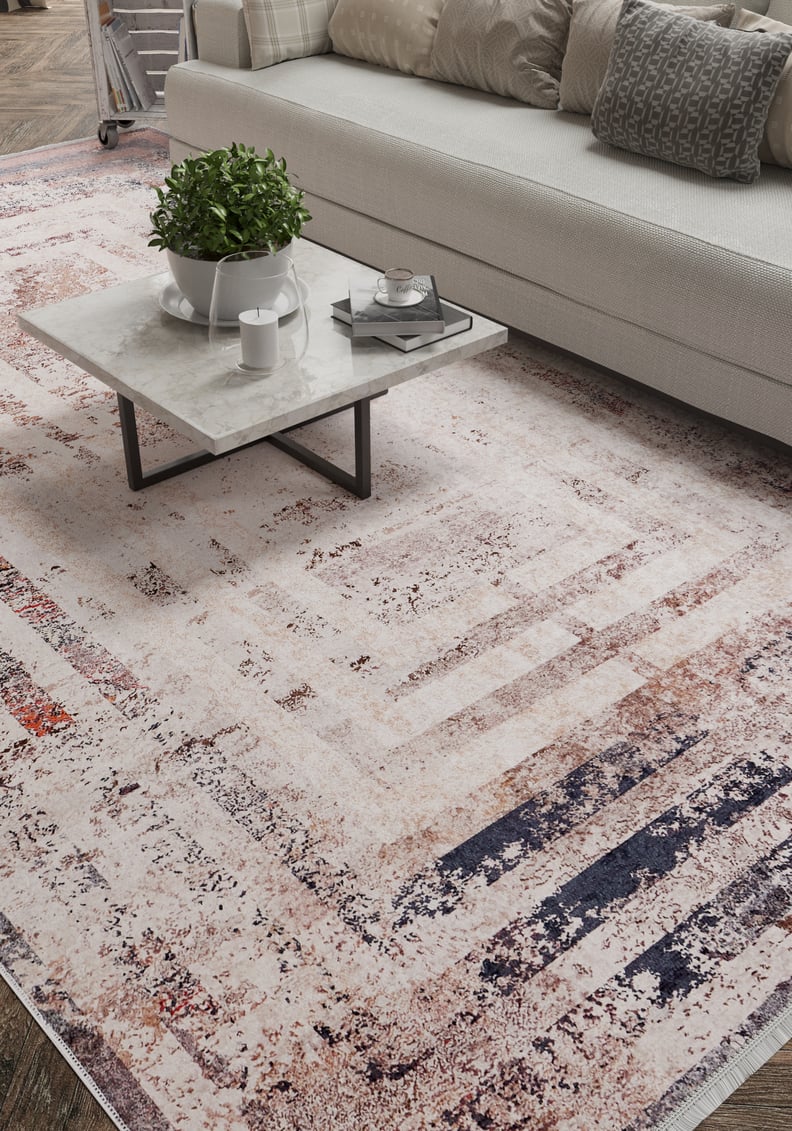 A modern living room features the Bold and Geometric - Washable Rug - JR1410, perfect for high-traffic areas, a square marble coffee table with a plant and cup, and a beige sofa accented by textured pillows in the background.
