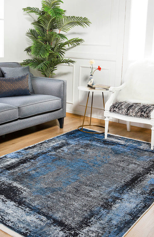 Load image 1 in gallery view. A living room with the Bold and Minimalist - Washable Rug - JR1229 (Custom Size) in blue, a gray sofa with pillows, white chair with blanket, small side table with flowers, and a tall green plant on a high-traffic wooden floor.