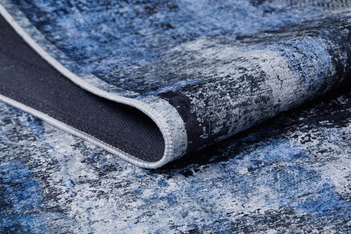 Load image 1 in gallery view. A close-up of the Bold and Minimalist - Washable Rug - JR1229 (Custom Size) shows its textured blue, distressed pattern. The image highlights the lifted edge to display detailed stitching and underside, ideal for high-traffic areas.