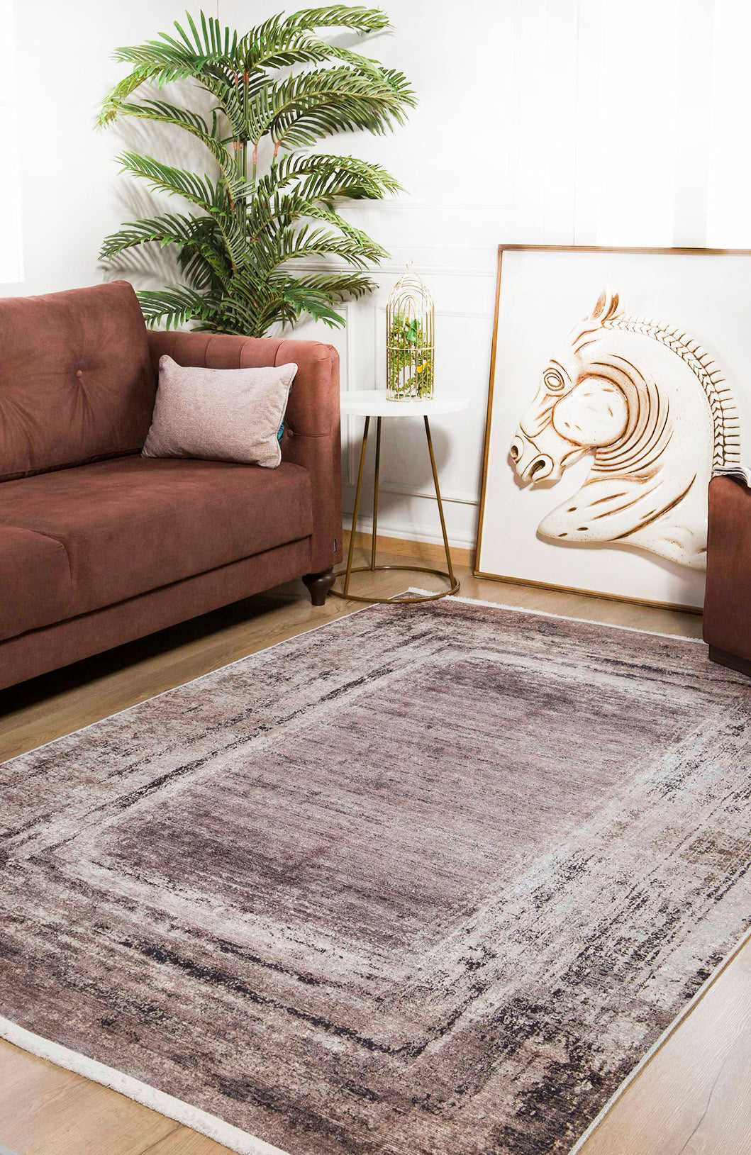 A cozy living room with a brown sofa, the Borderline Chic - Washable Rug - JR1156 (Custom Size) in gray-purple, a green plant, a side table featuring gold wire decor, and framed zebra art resting against the wall.
