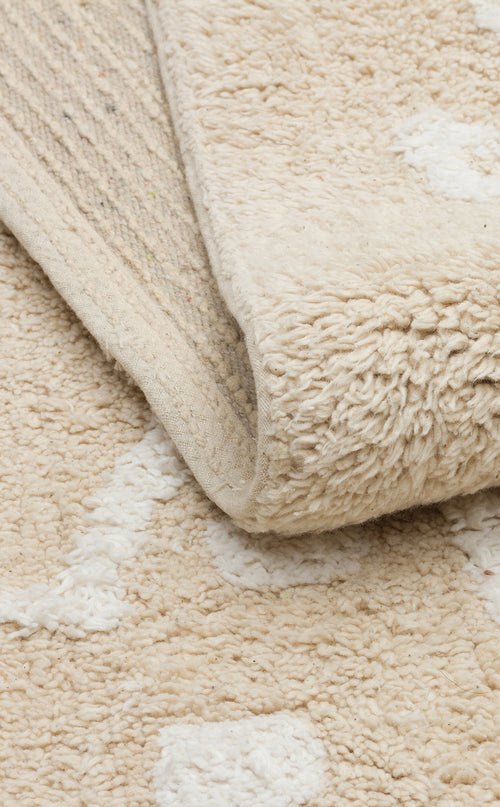 Load image 1 in gallery view. A close-up of the Calm Nest - Washable Shaggy - CBN16 rug in cream beige shows white patterns and a softly folded corner exposing its woven underside.