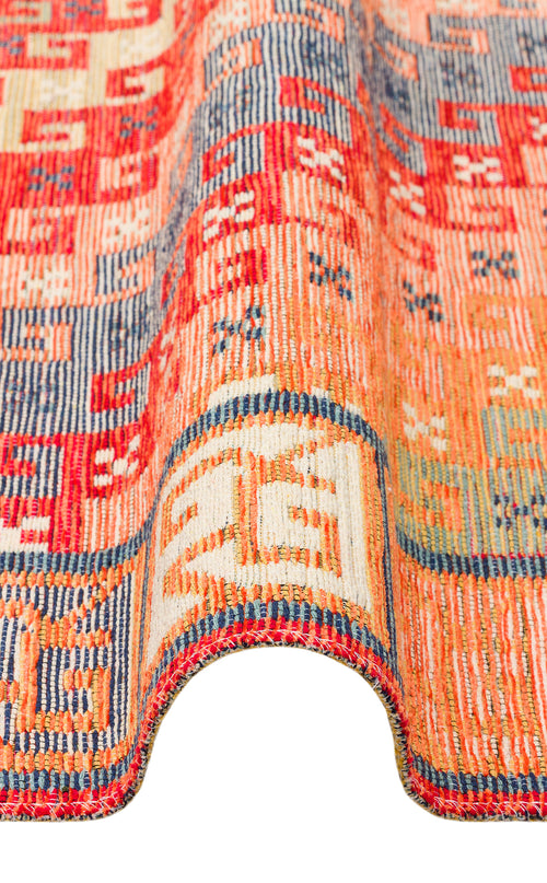 Load image 1 in gallery view. A close-up of the Canyon Shade - Washable Reversible Kilim - NMD11 showcases its vibrant red, orange, blue, and cream geometric patterns, elegantly draped in a wavy curve against a white background.