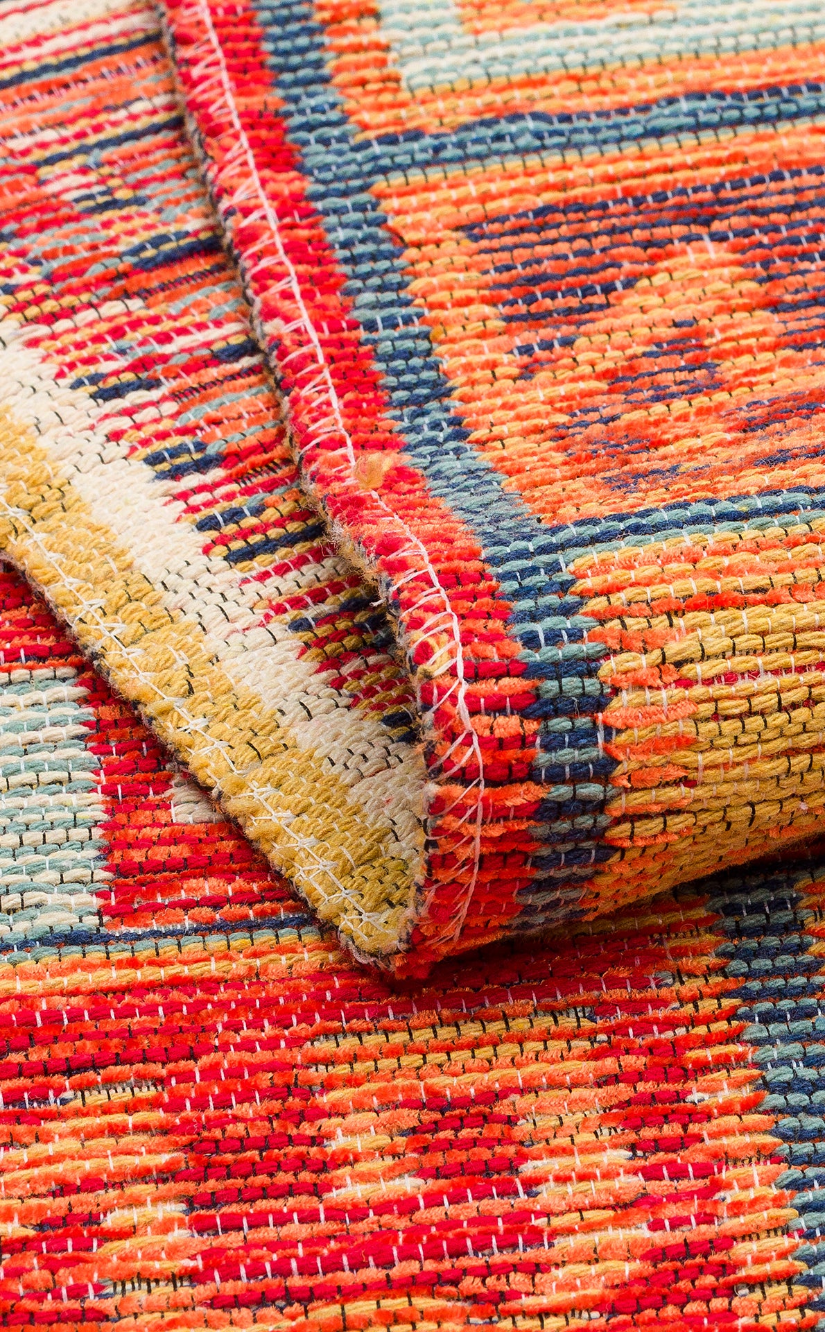 Close-up of the Canyon Shade - Washable Reversible Kilim (NMD11), featuring bold red, yellow, blue, and orange geometric tribal patterns. A folded corner reveals detailed stitching and texture on this vibrant washable rug.