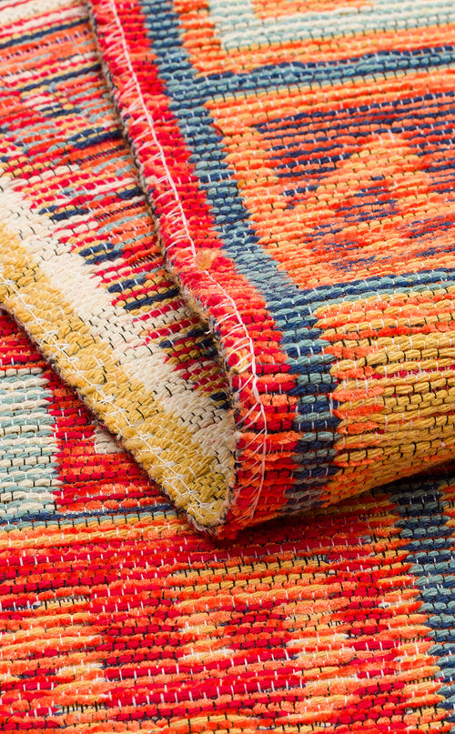 Load image 1 in gallery view. Close-up of the Canyon Shade - Washable Reversible Kilim (NMD11), featuring bold red, yellow, blue, and orange geometric tribal patterns. A folded corner reveals detailed stitching and texture on this vibrant washable rug.
