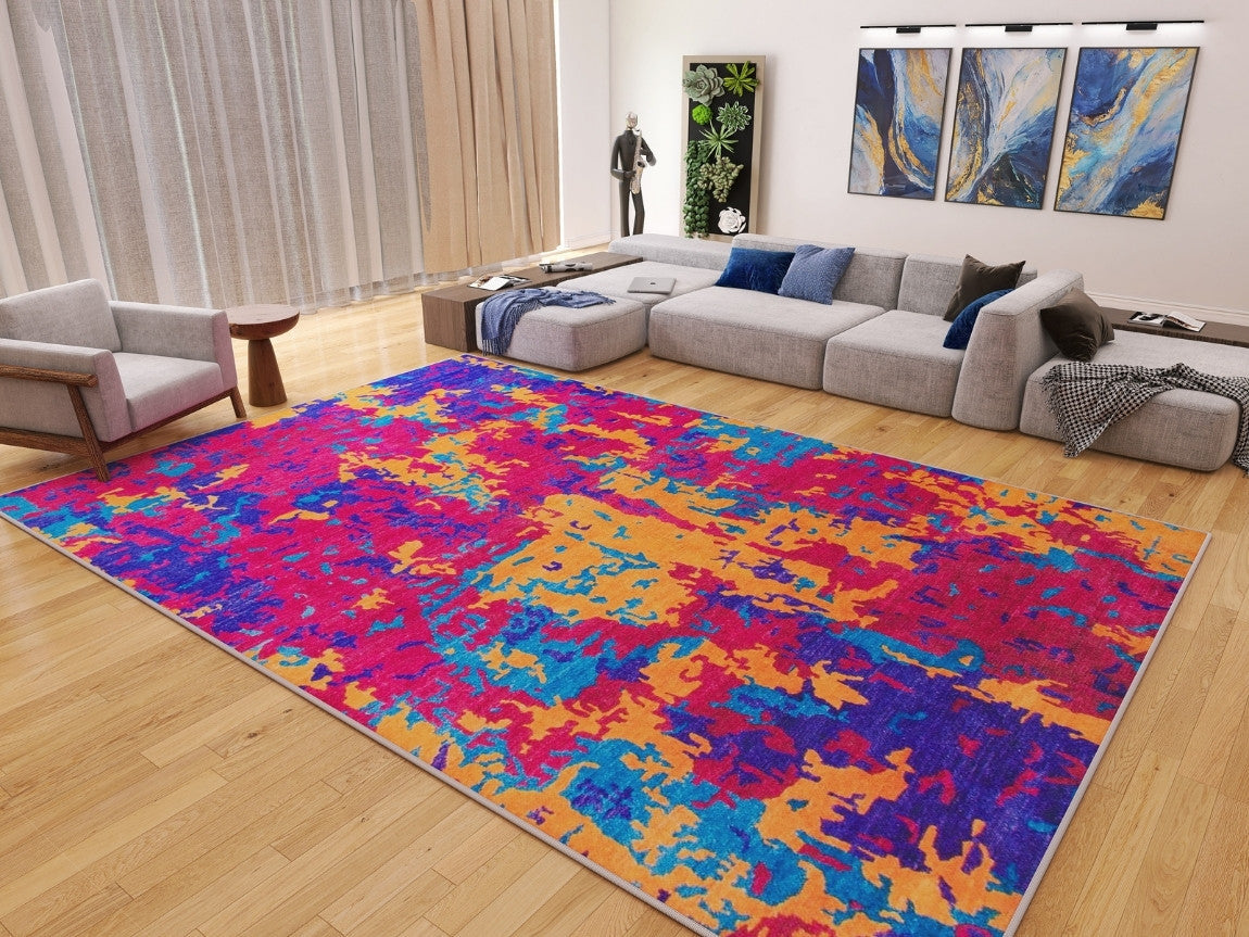 A modern living room with light wood floors, a Celestial Tapestry Washable Rug (JRS004) in bold colors—perfect for high-traffic areas—a gray sectional with blue pillows, wall art, plants, and floor-to-ceiling curtains.