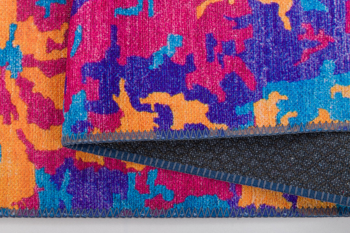 A close-up of the Celestial Tapestry - Washable Rug - JRS004 (Custom Size), featuring a colorful abstract pattern in pink, orange, blue, and purple. The folded edge reveals a dark underside with blue stitching—great for allergy-sensitive or busy spaces.