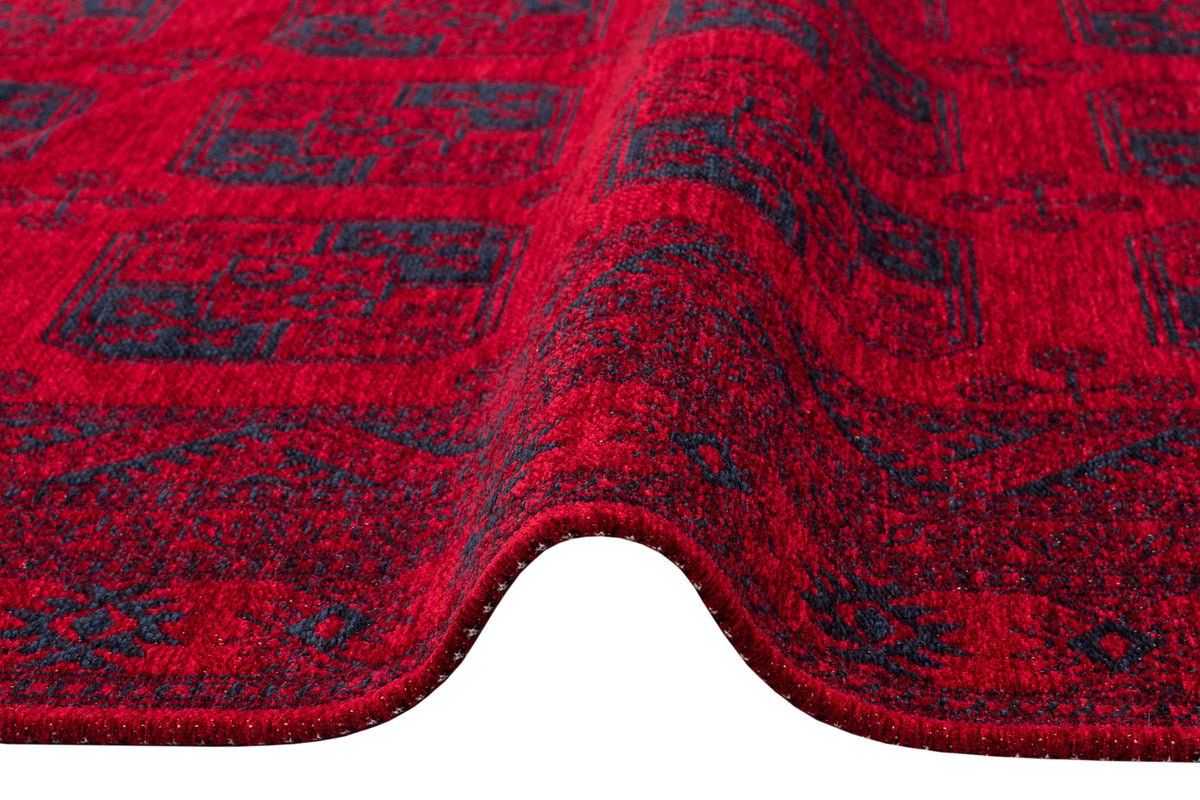 A close-up of the Cherry Texture - Washable Kilim - BHR01, featuring detailed red and dark blue geometric designs and texture with a wave-like fold, shown against a white background.