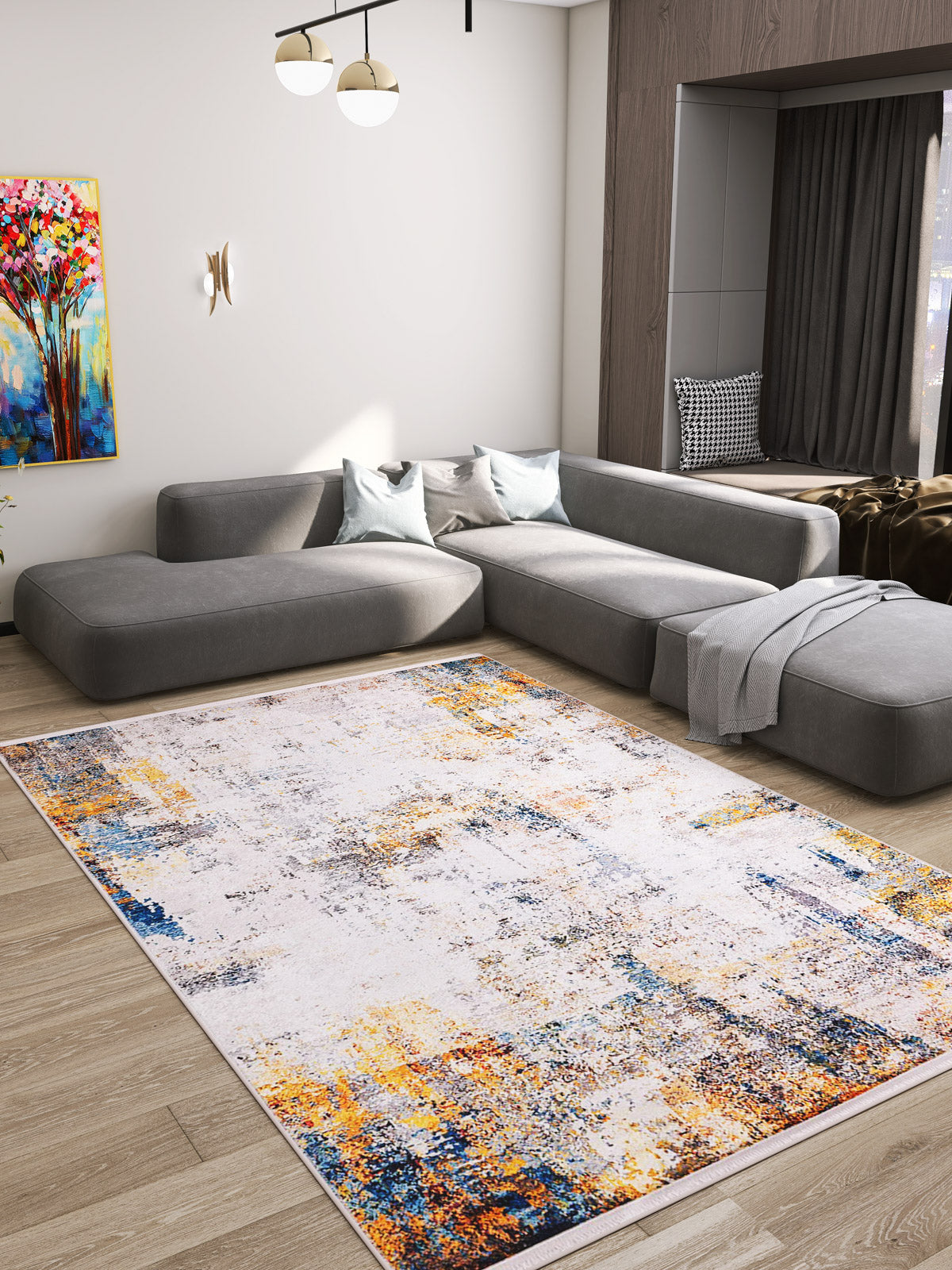 A modern living room features a large gray sectional sofa, light blue pillows, and the Chromatic Kaleidoscope - Washable Rug - JR1483 (Custom Size) with blue, orange, and yellow accents—ideal for high-traffic areas—complementing vibrant art and a wooden floor.
