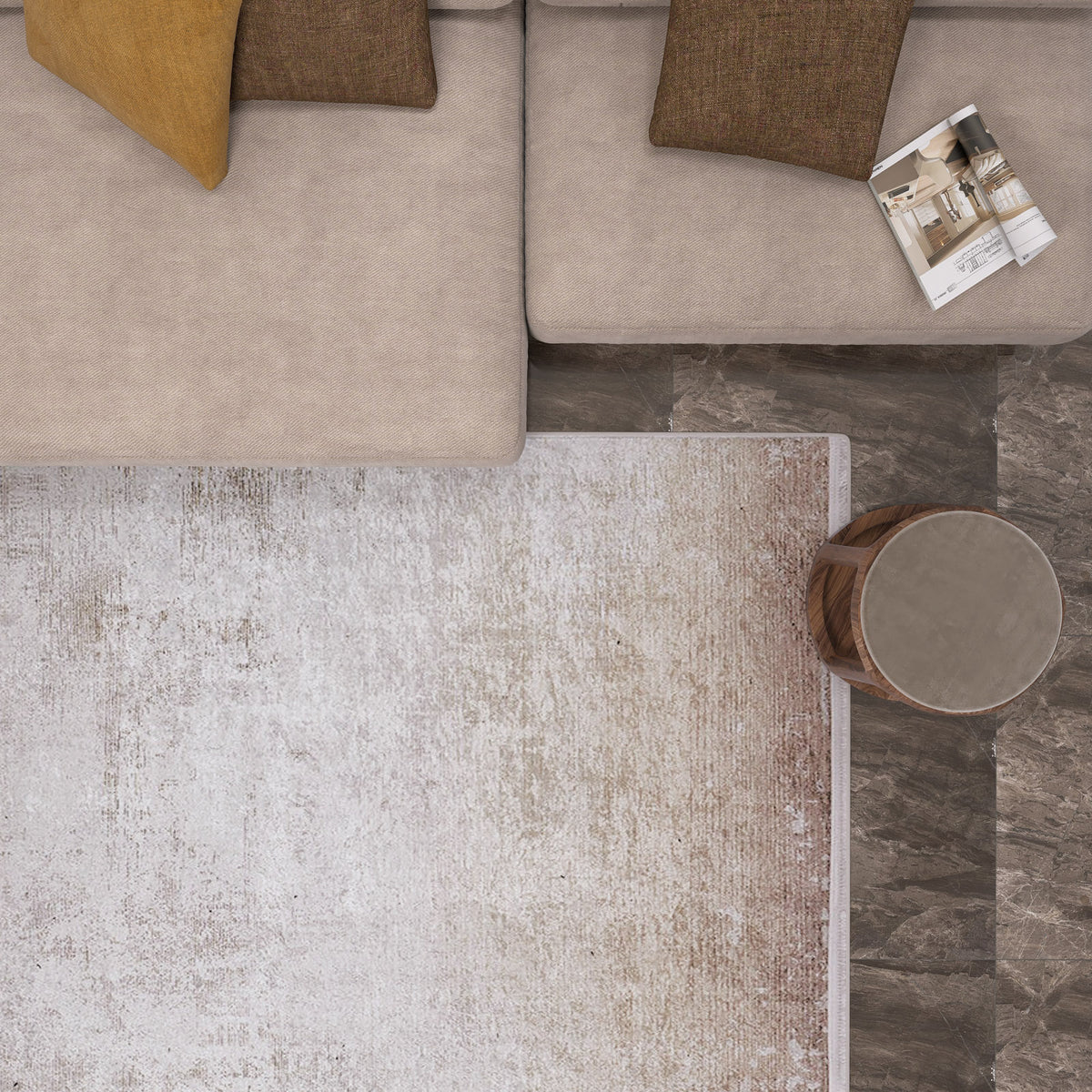 A top-down view of a beige sectional with brown and yellow pillows, an open magazine, a round wood side table, and the Cinnamon Swirl - Washable Rug - JR425—ideal for high-traffic areas—over dark marble-patterned flooring.
