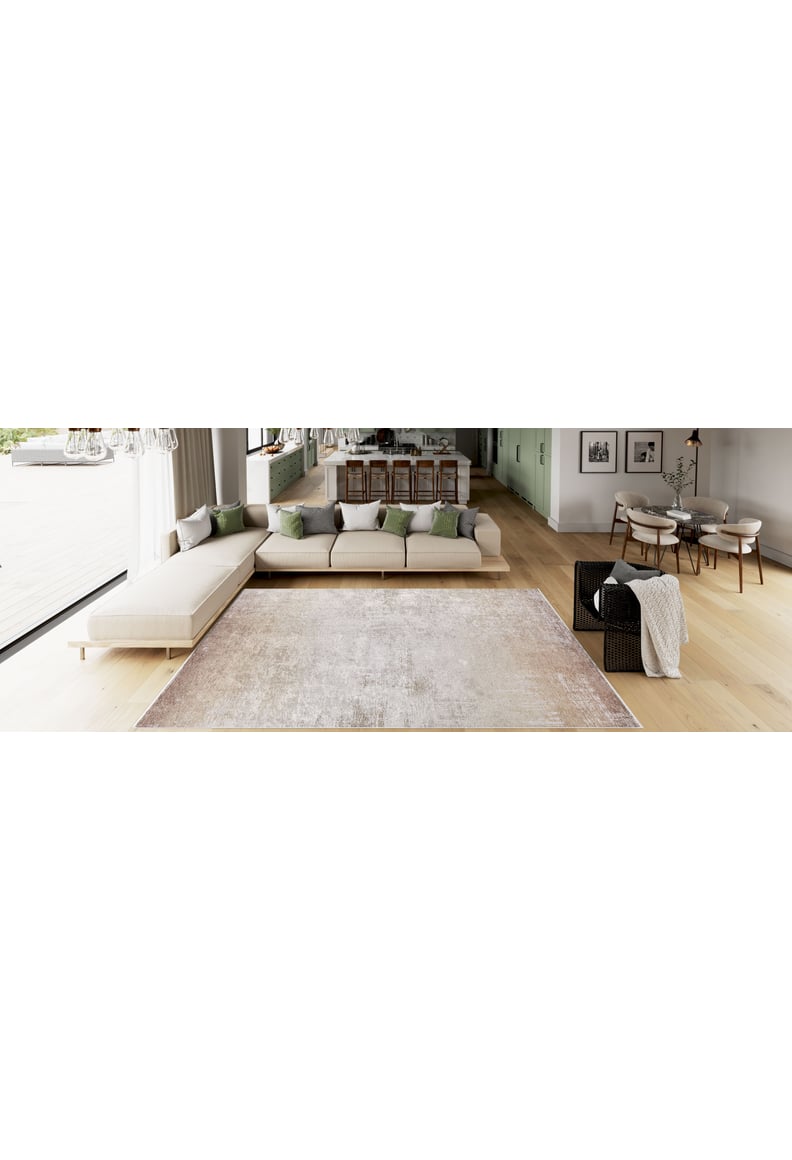 Modern living room with a large beige sectional, green and gray pillows, a Cinnamon Swirl - Washable Rug (JR425) ideal for high-traffic areas, a wicker chair, and an open dining area with a wooden table on light wood floors.