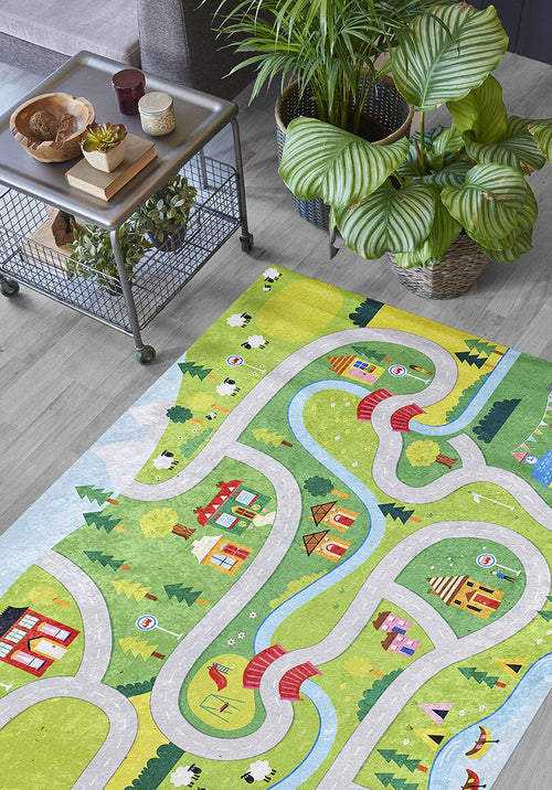 Load image 1 in gallery view. The City Adventure - Machine-Washable Rug JRC039 (Custom Size) adds color with winding roads, rivers, houses, trees, and animals—ideal for high-traffic areas—and is shown on a wooden floor beside a metal table with snacks and plants.