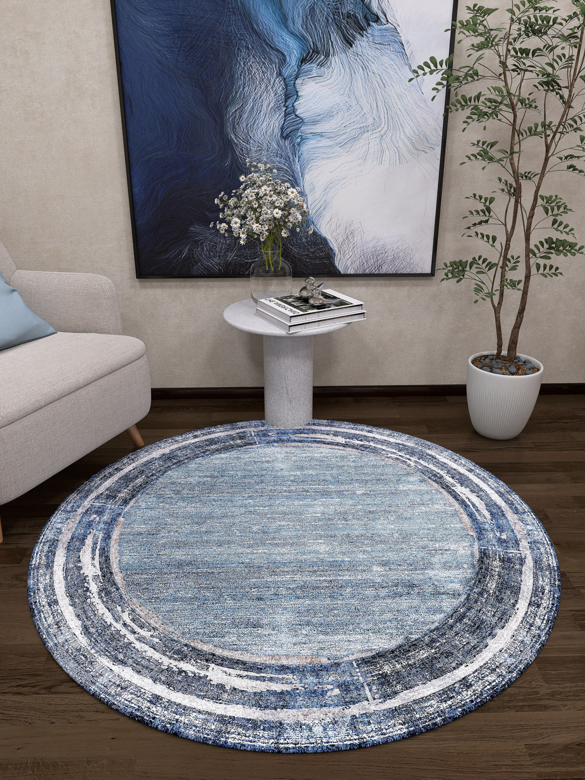 The Classic Bordered - Washable Rug - JR1197, in round blue and white, sits on a dark wood floor by a small table with flowers, a green potted plant, beige sofa with blue pillow, and abstract art—ideal for modern, high-traffic living rooms.