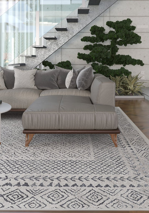 Load image 1 in gallery view. A modern living room features a gray sectional sofa with assorted pillows atop the Classic Contrast - Washable Rug - JR1985 (Custom Size), a potted plant, glass-railed staircase, and large windows letting in natural light.