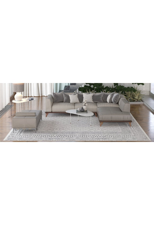 Load image 1 in gallery view. A modern living room features a gray sectional sofa, matching ottoman, white coffee tables, lamp, decorative plants near large windows with white curtains, and the Classic Contrast - Washable Rug - JR1985 (Custom Size) as a stylish flat weave rug.