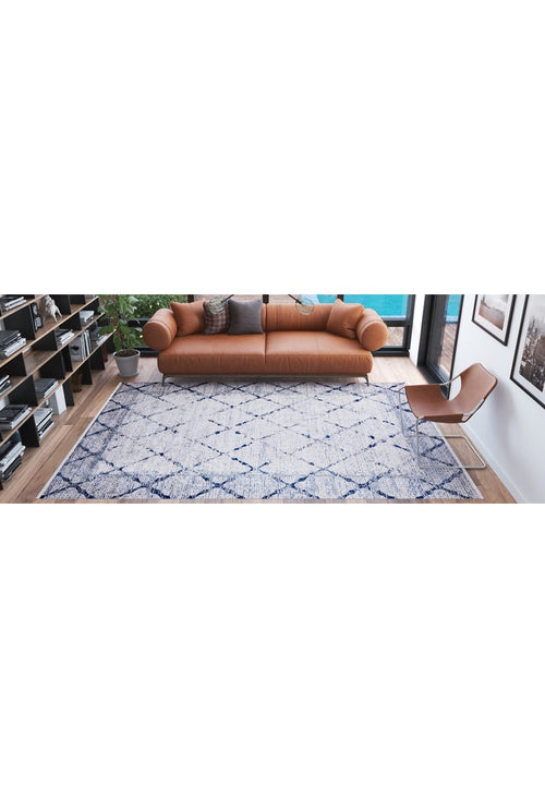 Load image 1 in gallery view. A modern living room with a tan leather sofa, brown chair, Classic Trellis - Washable Rug - JR710 in blue and white, bookshelves, a potted plant, and large windows letting in natural light.