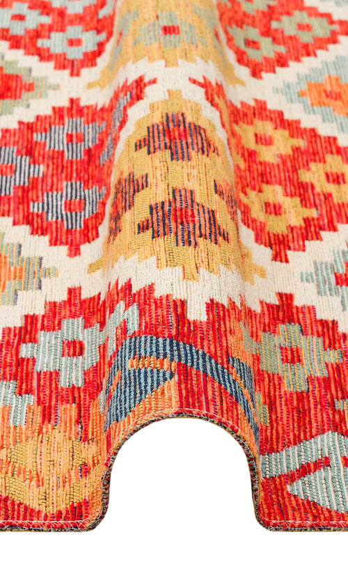 Load image 1 in gallery view. A close-up of the Clay Mark - Washable Reversible Kilim - NMD05 rug, featuring vibrant red, yellow, blue, and cream geometric patterns. The partial fold shows off its rich texture and thickness.