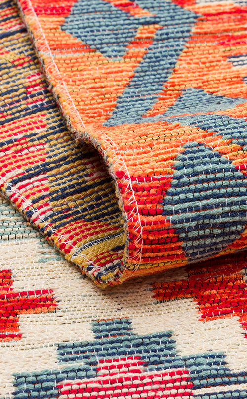 Load image 1 in gallery view. A close-up of the Clay Mark - Washable Reversible Kilim - NMD05 folded at the corner, showcasing geometric patterns in red, orange, blue, and yellow on a cream background with visible texture and stitching.