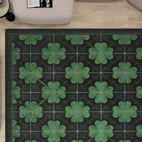 Load image 1 in gallery view. A top-down view of the Clover Noir - Washable Rug - JRS012, featuring a repeating green four-leaf clover pattern on a dark background, perfect for high-traffic areas, placed on light wood flooring near light chairs and an open magazine.