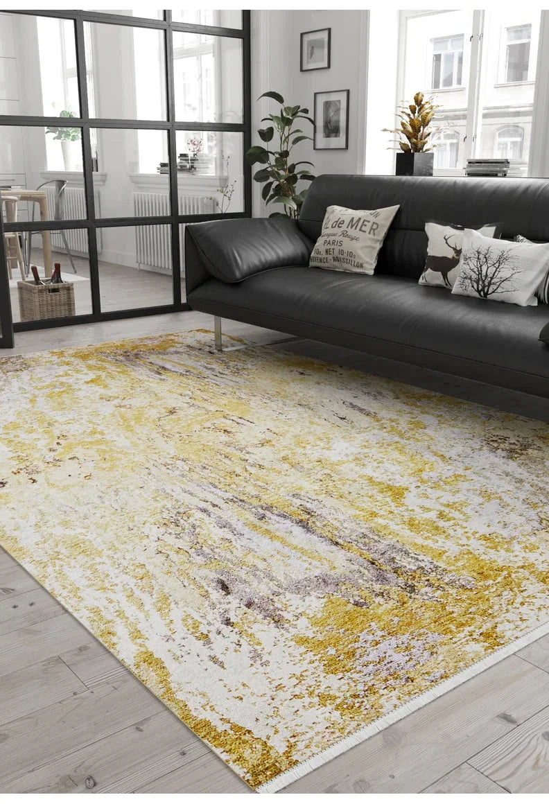 A modern living room with a black sofa, decorative pillows, a potted plant, and the Color Splash - Washable Rug - JR146 in yellow-gold on light wood flooring. Large windows let in natural light—ideal for high-traffic areas.