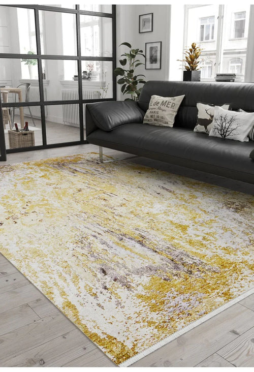 Bild 1 in Galerieansicht laden. A modern living room with a black sofa, decorative pillows, a potted plant, and the Color Splash - Washable Rug - JR146 in yellow-gold on light wood flooring. Large windows let in natural light—ideal for high-traffic areas.