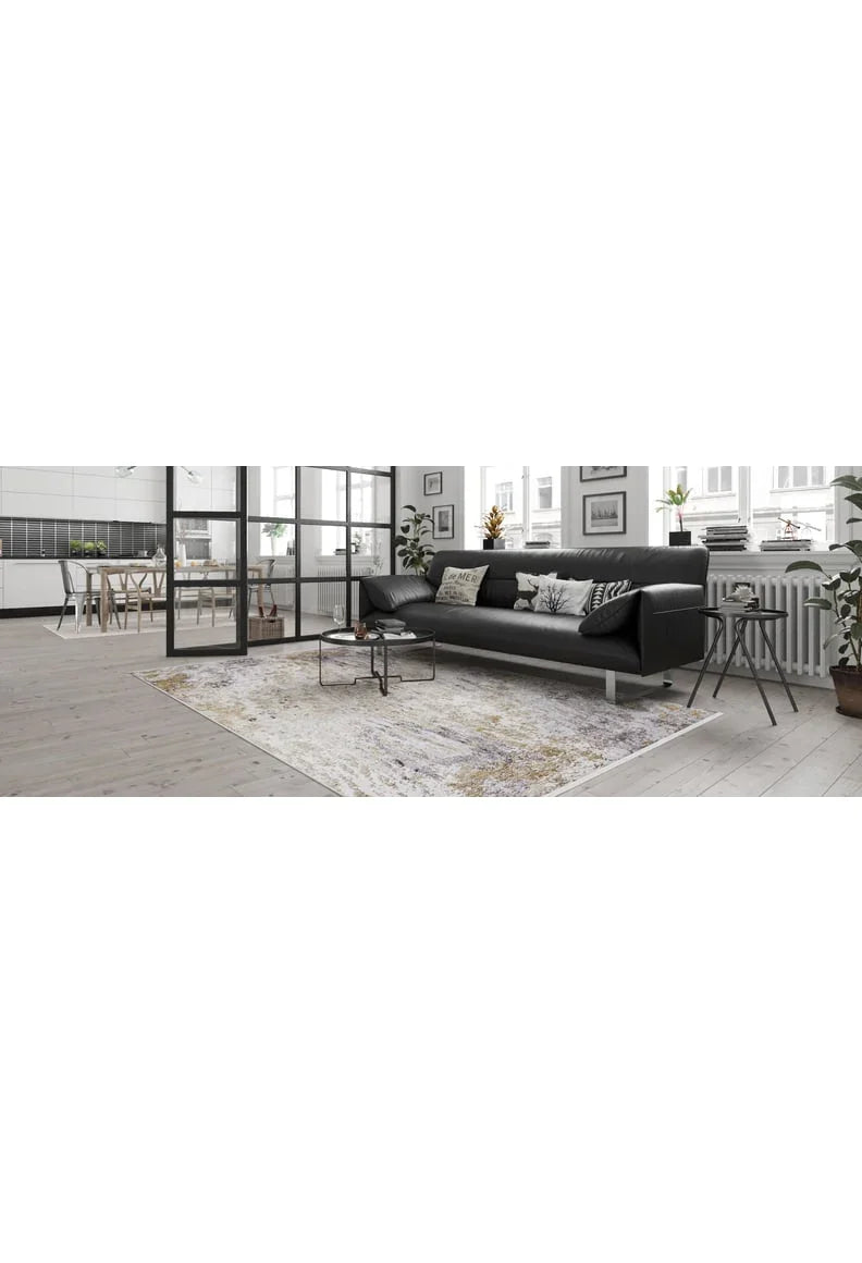 A modern living room features a black sectional sofa, patterned cushions, and the Contemporary Canvas - Washable Rug - JR145—ideal for high-traffic areas. Glass doors lead to the dining area and kitchen, with large windows bringing in natural light.