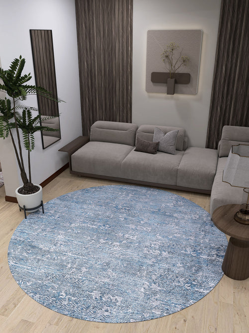 Load image 1 in gallery view. A modern living room with a gray sectional, wood-accented walls, wall art, a potted plant, and a small side table on light wood floors. The Contemporary Serenity - Machine-Washable Rug JR1884 in blue anchors the space and suits high-traffic areas.