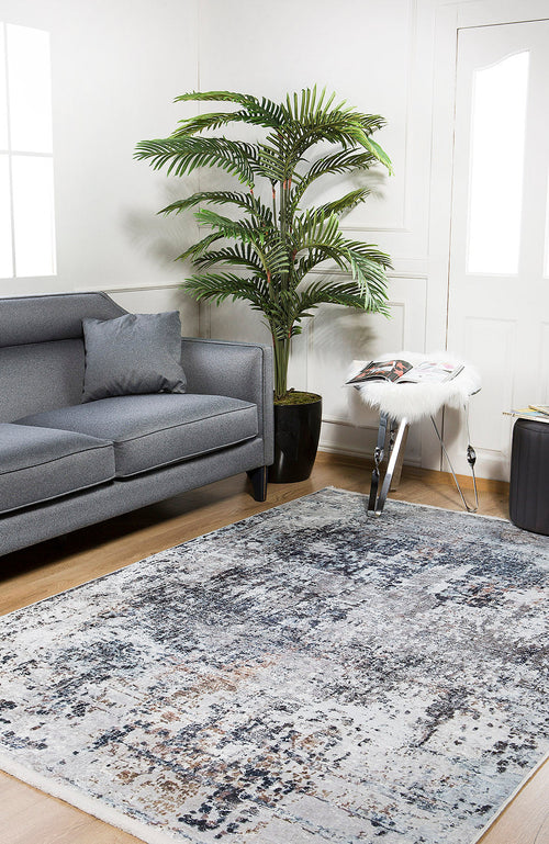Load image 1 in gallery view. A modern living room featuring a gray sofa, the Creative Currents - Washable Rug - JR835 (Custom Size), a tall potted plant, and a side table with a magazine, all set against white walls with windows and a wooden floor.