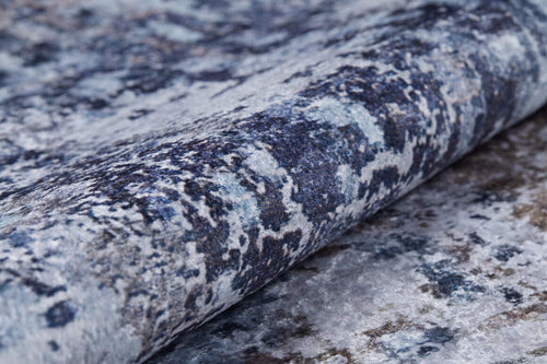 Load image 1 in gallery view. Close-up of the Creative Currents - Washable Rug - JR835 (Custom Size), showcasing its abstract marbled pattern in blue, gray, and white, partially rolled to display its plush thickness and detailed surface.