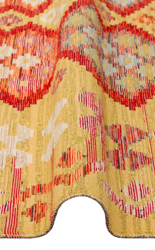 Load image 1 in gallery view. A close-up of the Crimson Dot - Kilim - NMD03 polyester flat weave rug features a yellow background with red and white geometric patterns and a wavy, folded edge.