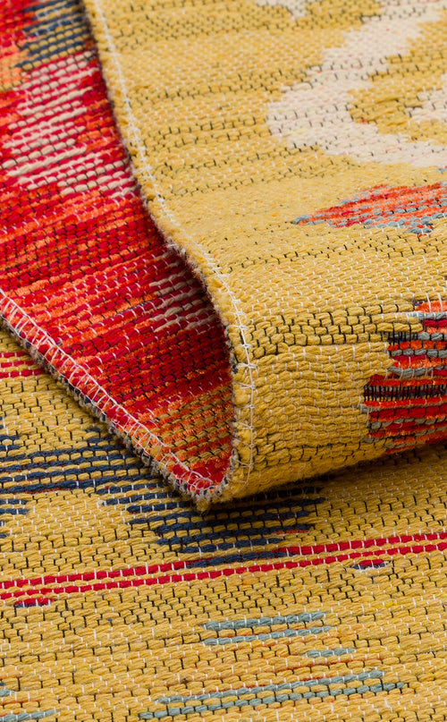 Load image 1 in gallery view. A close-up of the Crimson Dot - Kilim - NMD03 rug shows its folded corner, emphasizing the yellow background with red, blue, and beige patterns as well as its detailed texture and stitching.