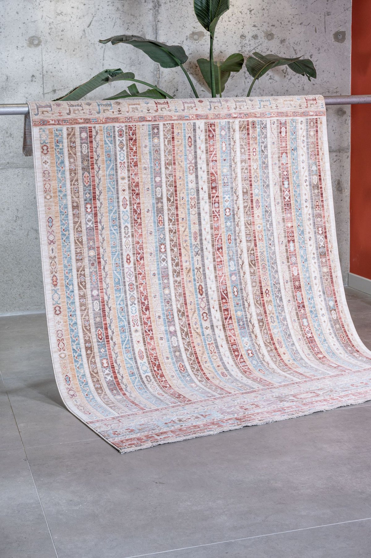 Multi-colored striped rug with intricate geometric patterns in blue, red, and beige, draped over a rail in a studio.