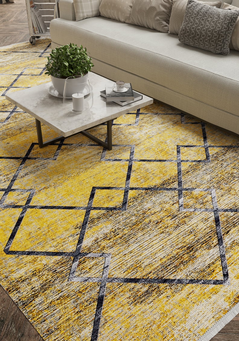 A modern living room features a white sofa, grey patterned pillows, and a marble coffee table with decor. The floor showcases the Crossed Connections - Washable Rug - JR1181 (Outlet) US in yellow-gold with navy geometric lines—ideal for busy spaces.
